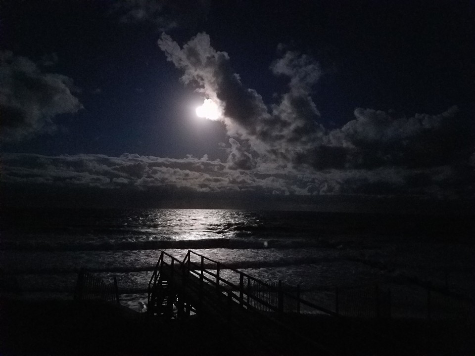 full moon peeking through clouds reflected on the ocean at night